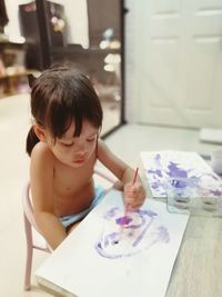 Shirtless girl painting on paper at table