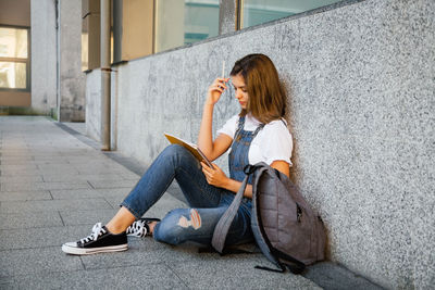 Full length of young woman sitting on wall