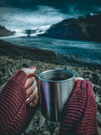 Cropped hands of woman having drink in cup at riverbank during winter