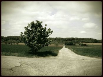 Road passing through field against cloudy sky