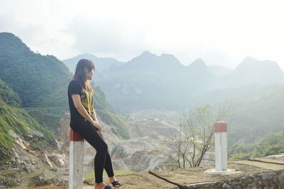 Side view of young woman standing on mountain against cloudy sky