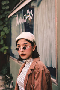 Portrait of young woman standing against window