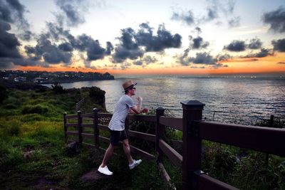 Man photographing on railing against sky during sunset