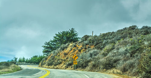 Road by trees against sky