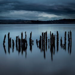 Wooden posts in sea against sky at dusk