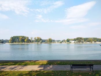 Bench by river against sky