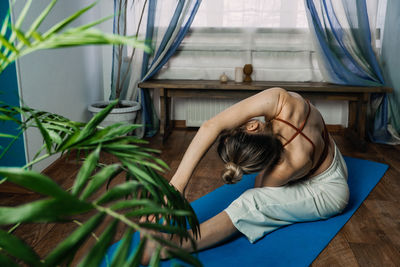 Back view of young woman in sportswear sitting in lotus position while doing yoga at home