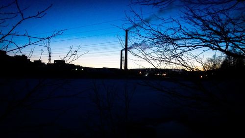 Silhouette trees and electricity pylon against sky at dusk