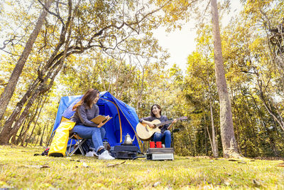 Happy friends with book and guitar camping in forest