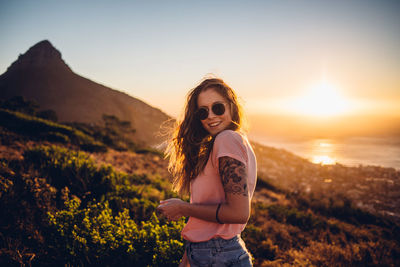 Beautiful young woman standing on land against sky during sunset