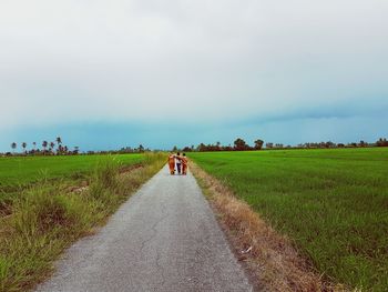 Rear view of people on road amidst field against sky