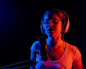 Portrait of young woman with microphone against black background