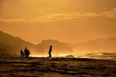 Silhouette people on beach against sky during sunrise