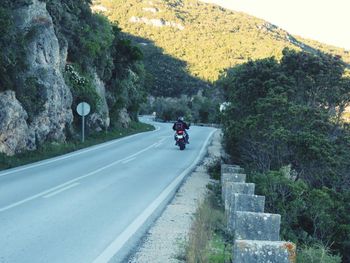 Rear view of man riding motorcycle on road against mountain