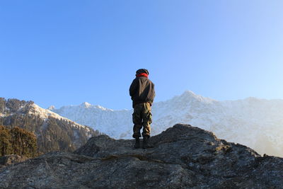 Rear view of man on rock against clear blue sky during winter