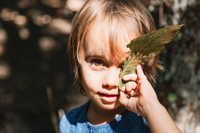 Close-up portrait of girl holding leaf in forest