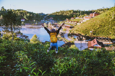 Rear view of woman jumping over plants against sky