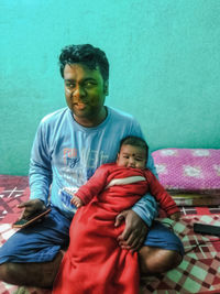 Full length of father with baby sitting on sofa