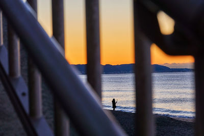 Silhouette people standing by railing against sea during sunrise