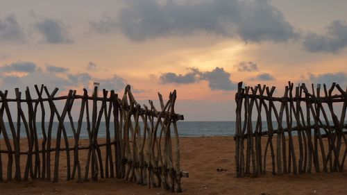 Wooden fence at beach against cloudy sky at dusk