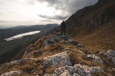 Man standing on rock by mountains against sky