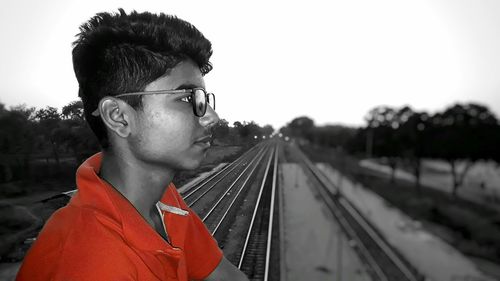 Portrait of young man looking at train against sky