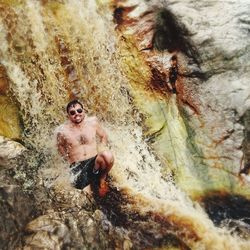 Shirtless man in waterfall against rock formation