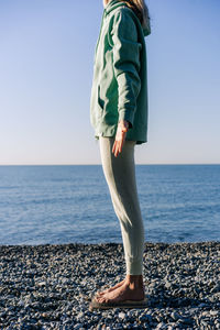 Anonymous woman standing on boards with nails doing energy yoga practice on the seashore.