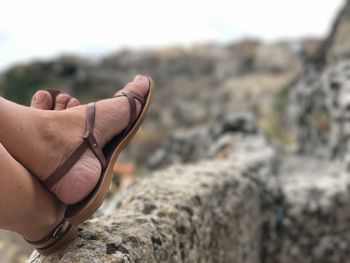 Low section of woman wearing scandals resting on retaining wall