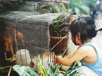 Girl sitting by bird in cage at yard