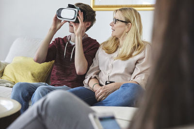 Mother looking at son using virtual reality headset while sitting on sofa