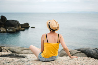 Rear view of man sitting on rock by sea