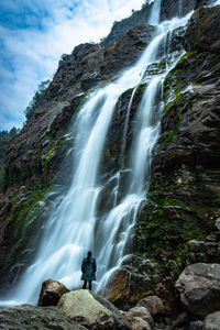 Waterfall white water stream falling from mountains with girl standing nearby at day