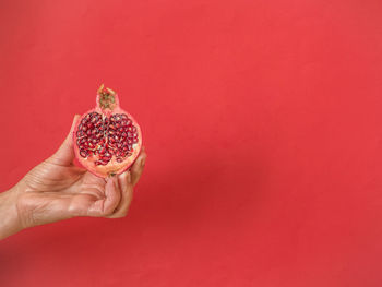 Hand holding half pomegranate on red background with copy space