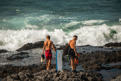 Rear view of shirtless man standing on rock in sea