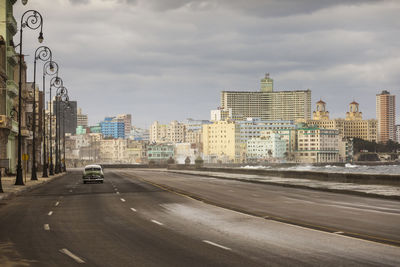 Cars on road by buildings in city against sky