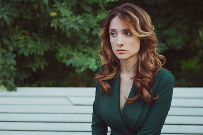 A young adult brunette woman is sitting on a bench in a green dress.