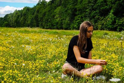 Teenage girl sitting amidst yellow flowers blooming on field