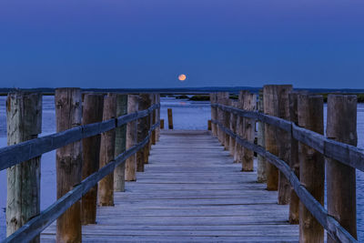 Boardwalk over sea against clear blue sky