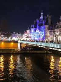 Illuminated bridge over river against buildings at night