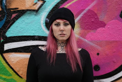 Portrait of smiling woman with pink hair standing against graffiti wall