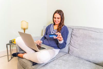 Smiling woman holding credit card while using laptop at home