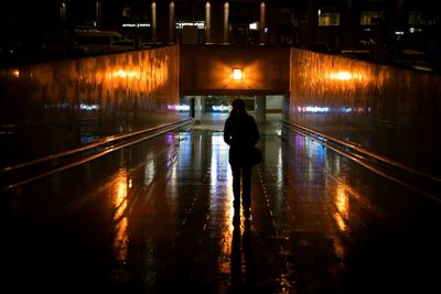 Rear view of silhouette woman walking on illuminated road at night