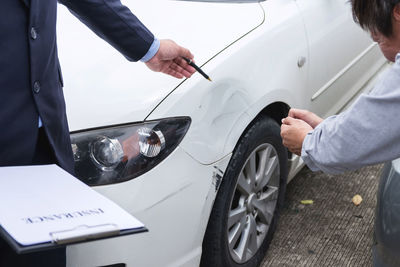 Midsection of businessman pointing at tire to mechanic