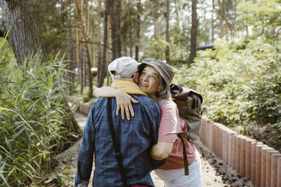 Happy senior woman hugging man while hiking in forest