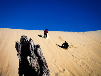 People riding on desert against clear blue sky