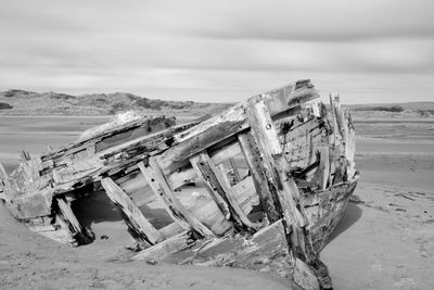 Damaged boat on beach against cloudy sky