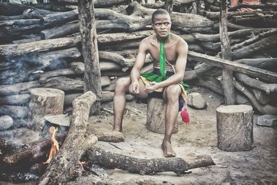 Full length of young man in traditional clothes sitting on log