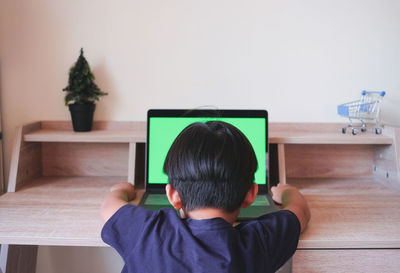 Rear view of boy sitting on table at home