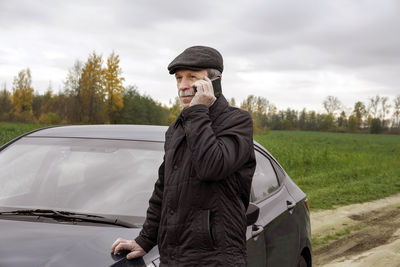 Man looking away while standing by car against sky